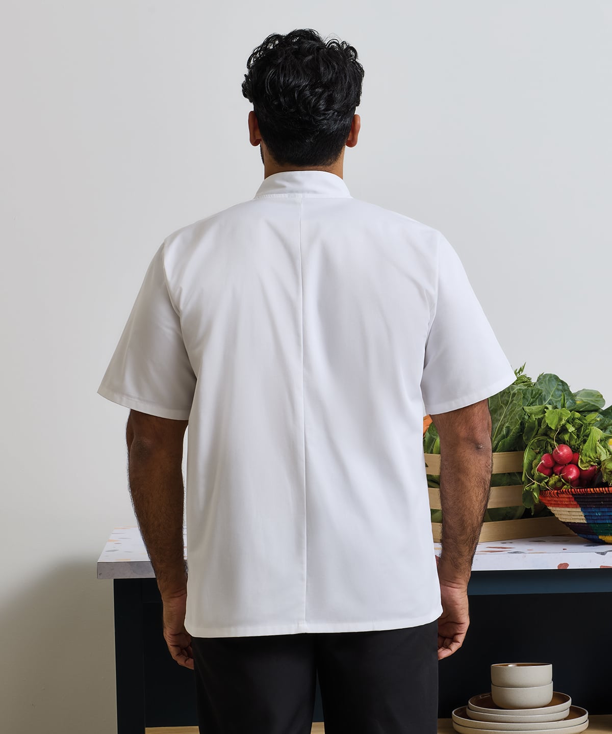 Chef wearing a white Short Sleeves Chef Jacket standing in front of a table with vegetables and kitchen items.