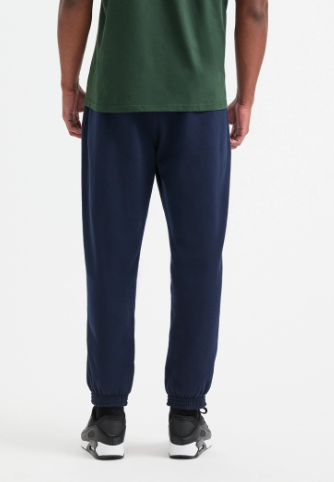A person shown from the back wearing dark navy jogger sweatpants, a green t-shirt, and black sneakers against a plain white studio background.