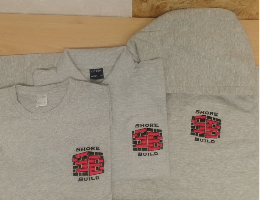 Gray t-shirt with 'Shore Build' logo on a wooden surface