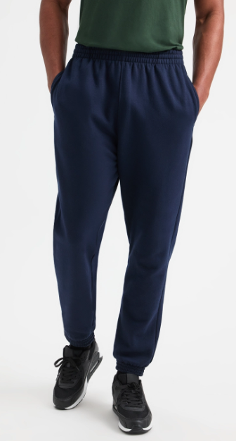 A person wearing navy blue jogger sweatpants with an elastic waistband and cuffs, paired with a green shirt and black sneakers, shown from the waist down on a light gray studio background.