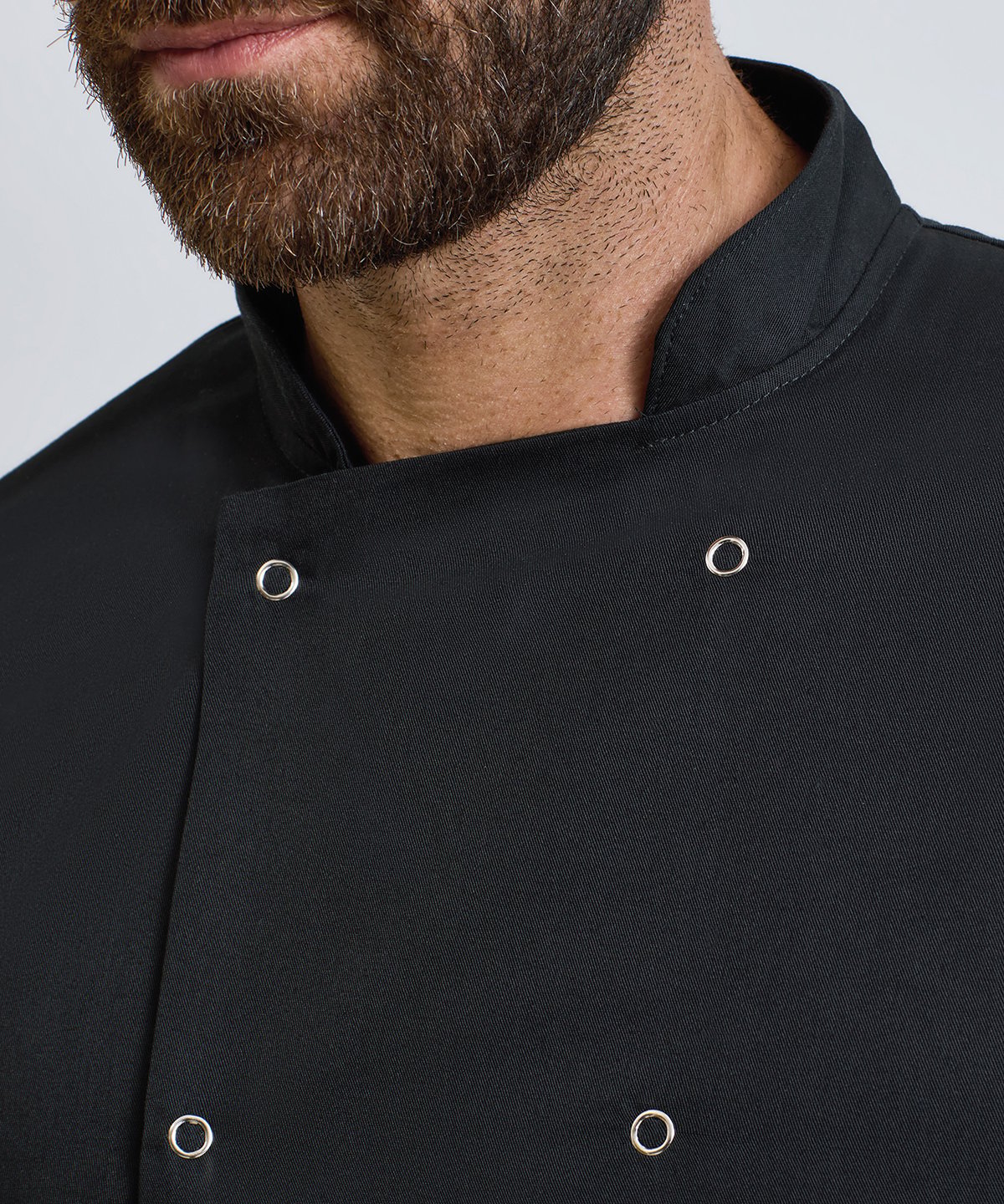 Close-up of a person wearing a black chef's coat with white buttons on a plain background